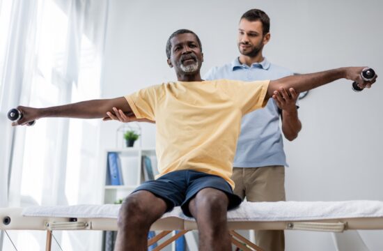 a photo of a physical therapist and his patient, who is sitting on a table with arms stretched wide holding weights